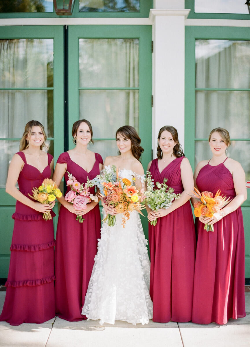 A bride is surrounded by her four bridesmaids, who wear ruby red dresses. All five women carried unique bouquets at this art-inspired wedding.