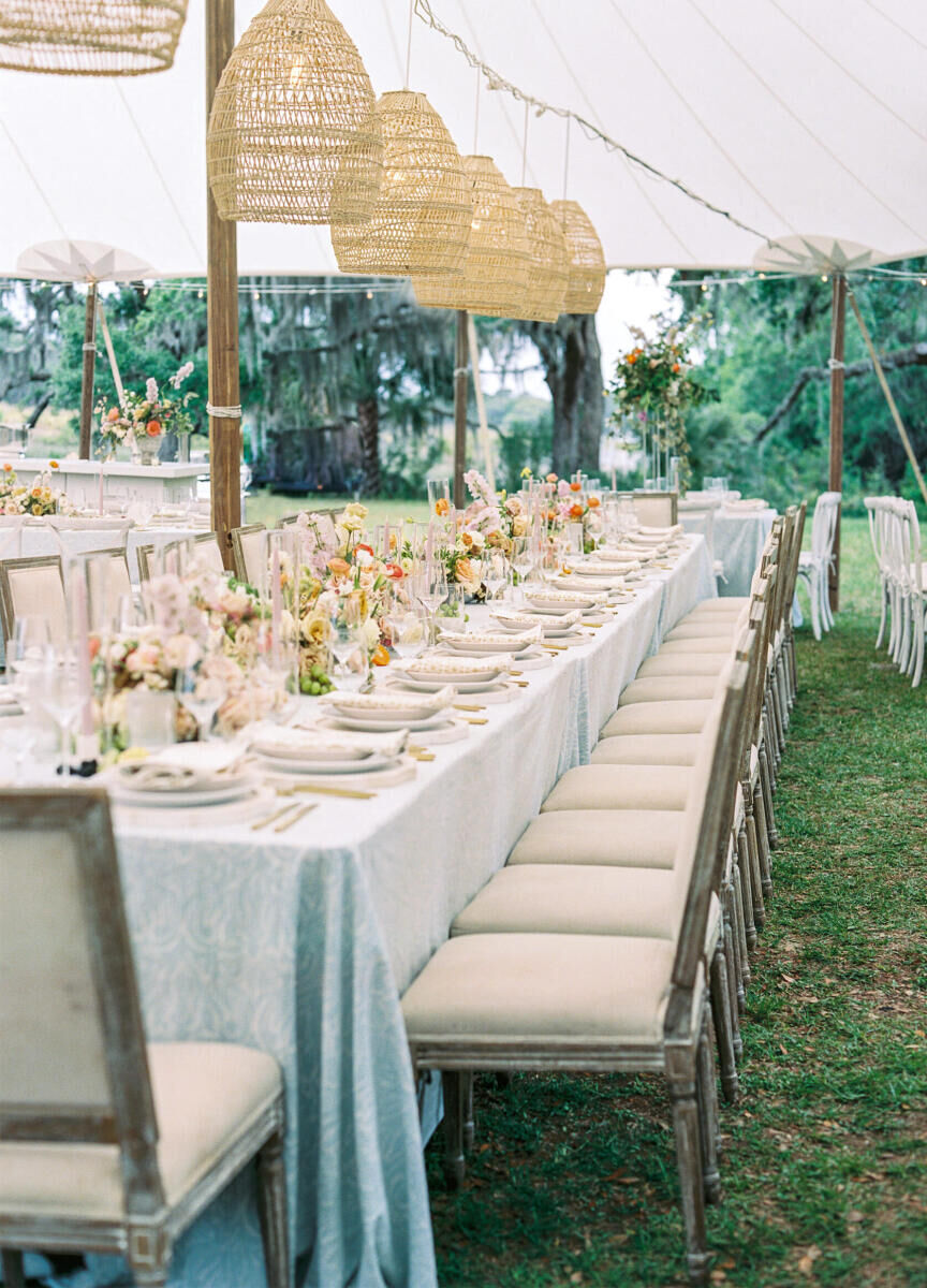 Woven light fixtures hung over long tables set with pale blue linens and upholstered chairs at an elegant spring wedding reception.