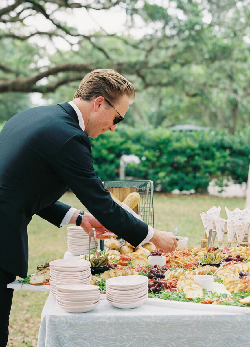 A guest serves himself at a grazing table set out during the cocktail hour of an elegant spring wedding.